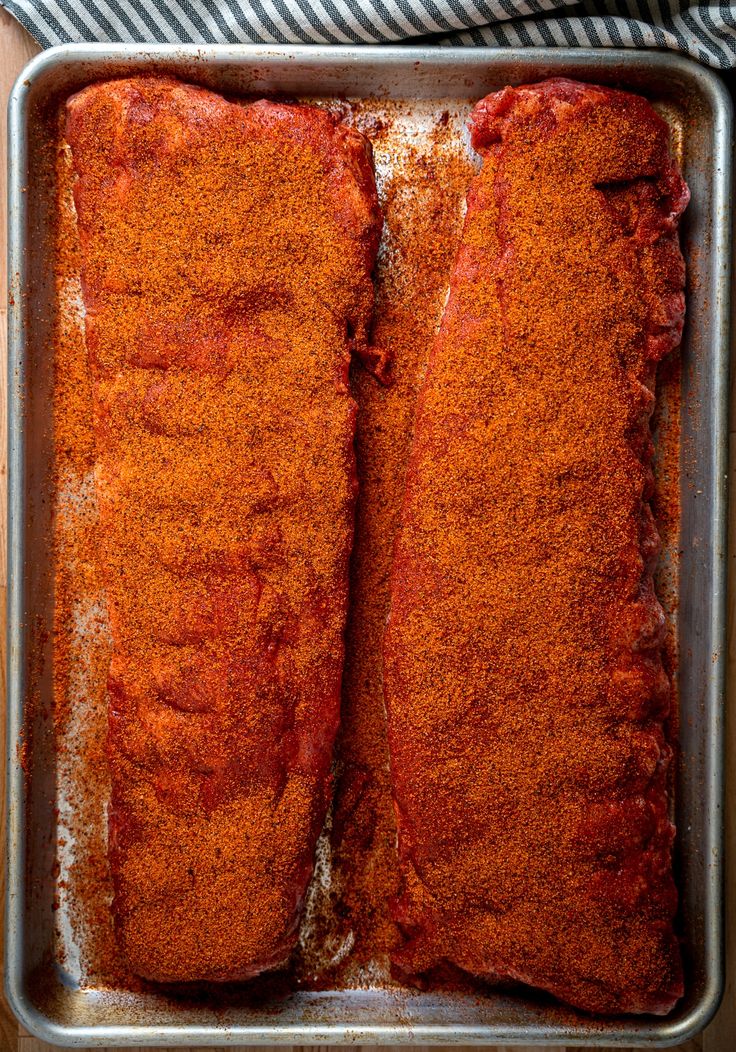 two pieces of meat in a metal pan covered with seasoning and pepper flakes