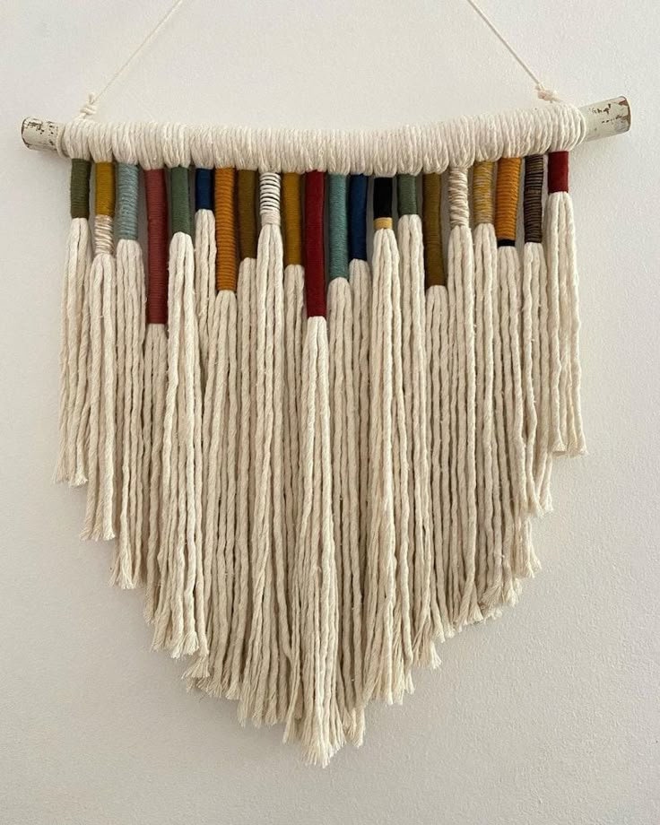 a white wall hanging with multicolored tassels on it's sides