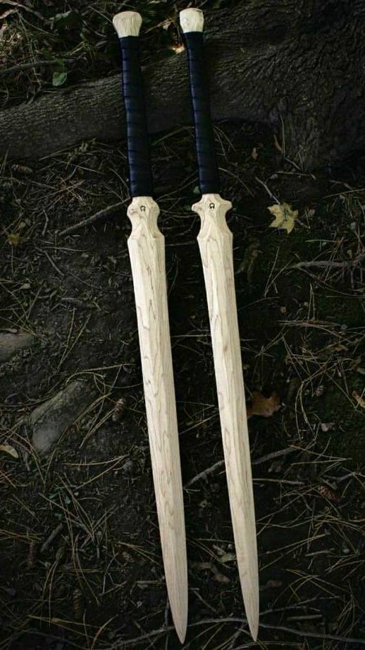 two wooden swords laying on the ground next to each other with black handles and white tips