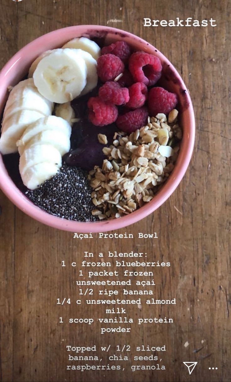 a pink bowl filled with granola, bananas and raspberries on top of a wooden table