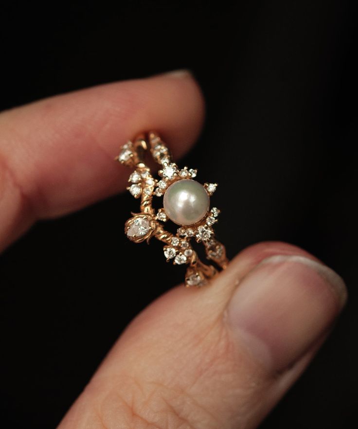 a close up of a person's hand holding a ring with pearls and diamonds