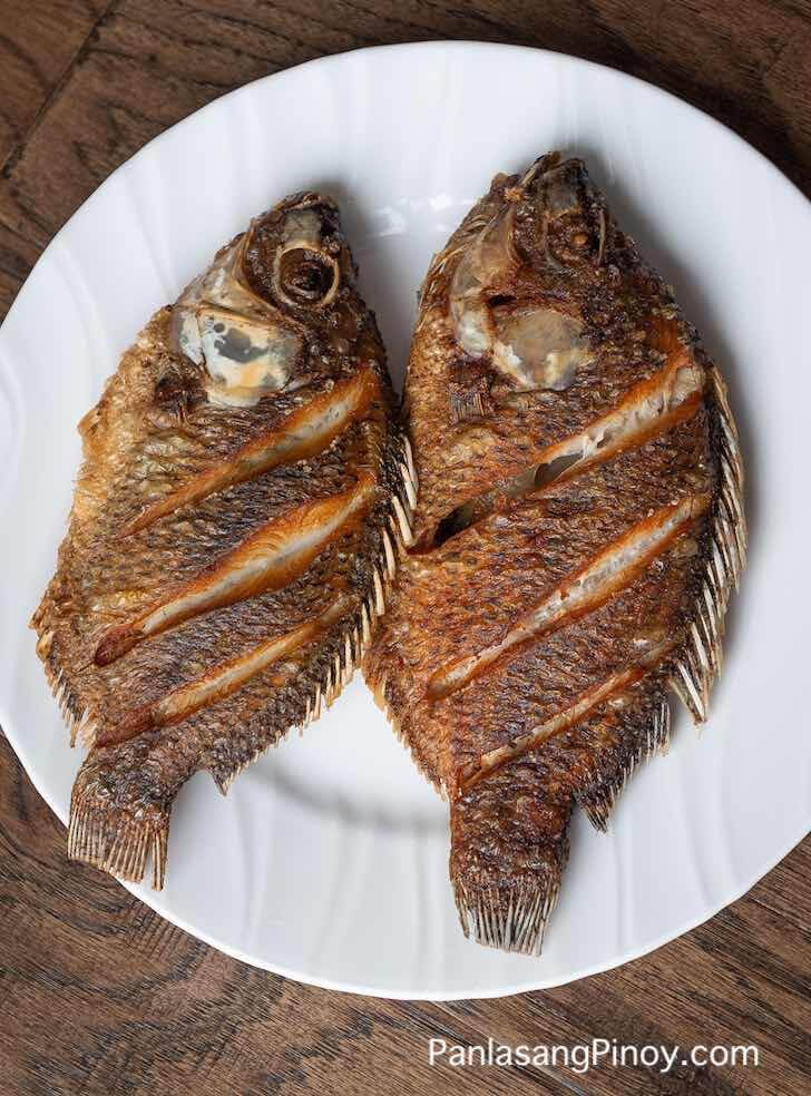 two fish are sitting on a white plate with brown wood flooring in the background