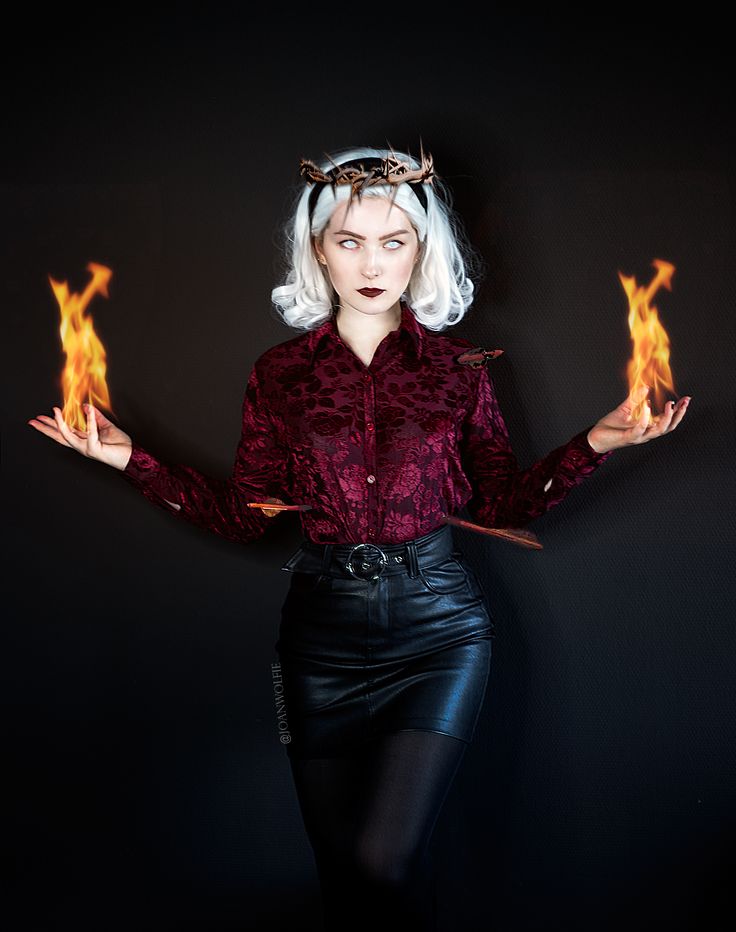 a woman with white hair wearing a red shirt and black leather skirt holding two flames in her hands