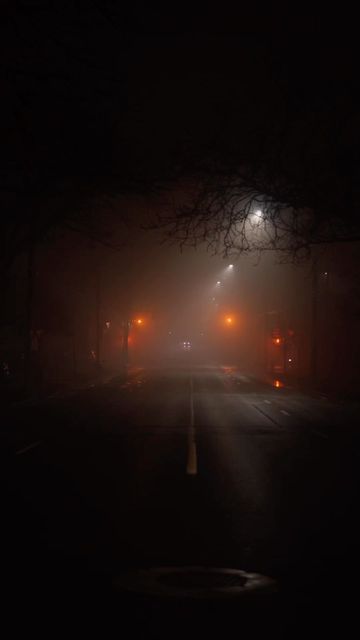 a dark street at night with lights on and fog in the air over cars driving down it