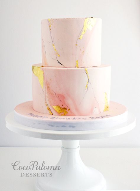 a three tiered cake with pink and gold marbled icing on a white pedestal