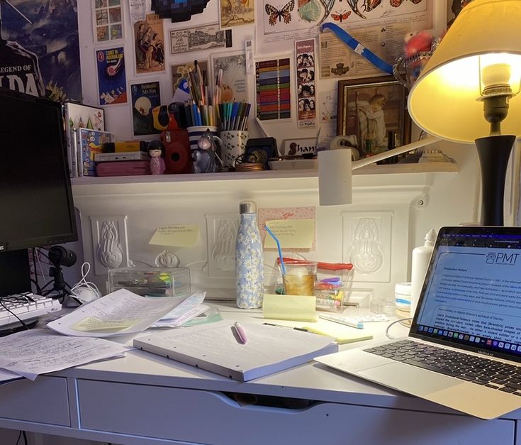 an open laptop computer sitting on top of a desk next to a lamp and papers