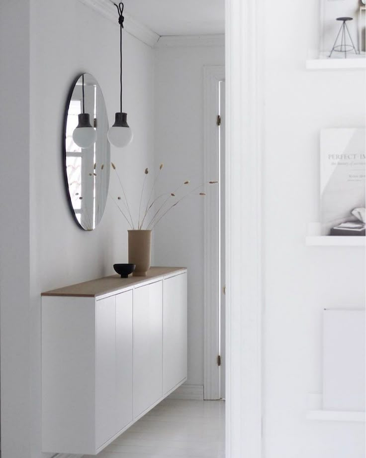 a white room with a mirror, vase and plant on the sideboard in front of it