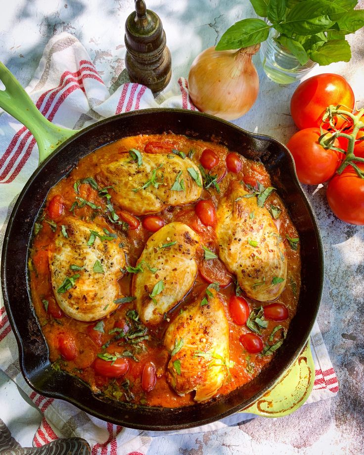 a pan filled with chicken and tomatoes on top of a table next to some vegetables