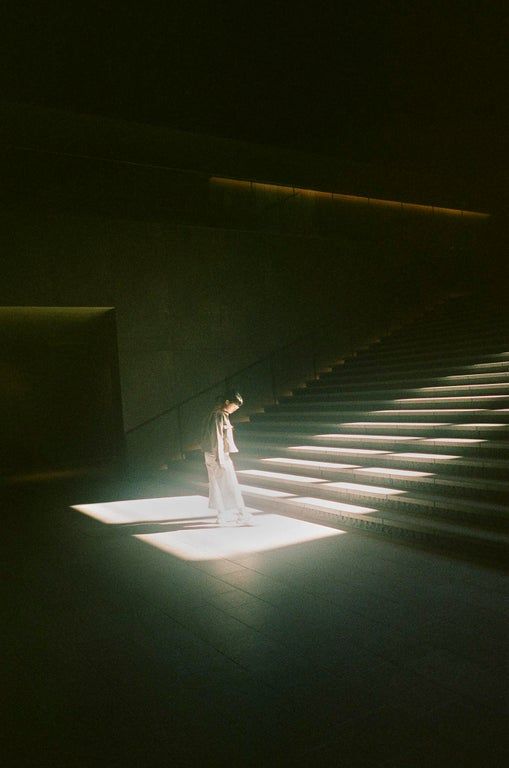 a woman standing in front of some stairs with her hand on her head and light coming through the window