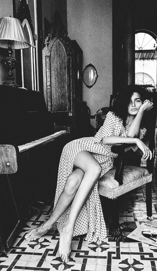 a woman sitting on a chair in a living room next to a piano and table