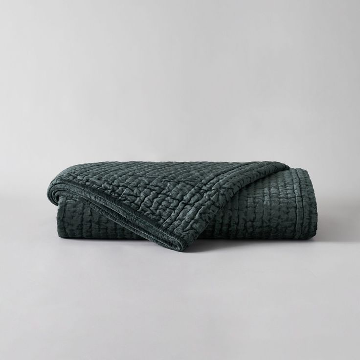 a dark green quilted blanket folded on top of a white table with grey background