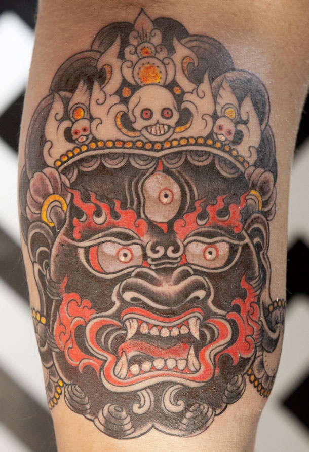 a close up of a person with a tattoo on his leg and the head of a demon