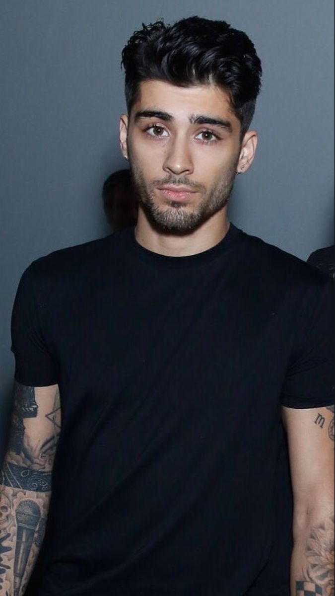 a man with tattoos standing next to a wall