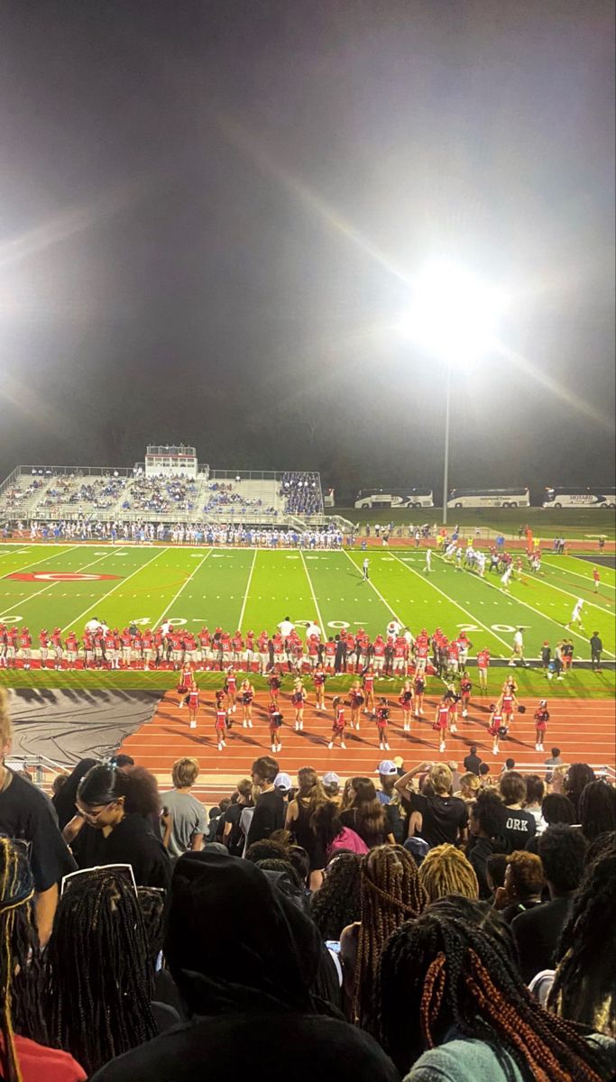 a football stadium filled with lots of people watching the game at night and some fans sitting on the bleachers