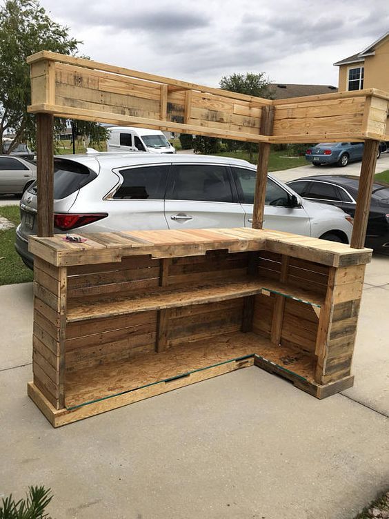 an outdoor bar made out of pallets and wood with cars parked in the background