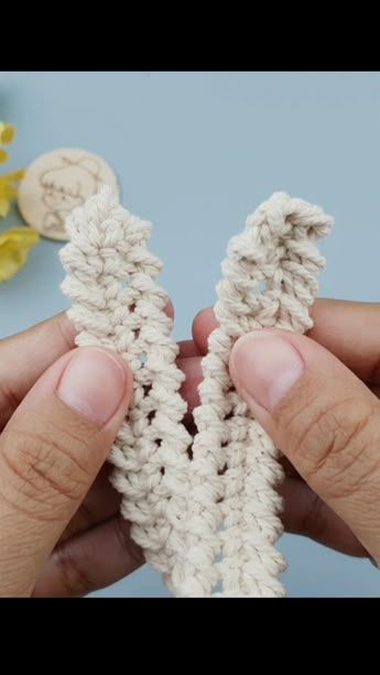 two hands holding crocheted pieces of yarn in front of some flowers and buttons