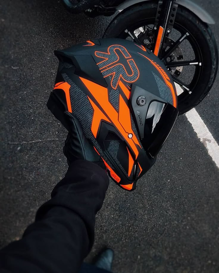 an orange and black motorcycle helmet sitting on the back of it's owner's hand