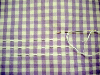 a pair of scissors is laying on a purple and white checkered tablecloth with stitching