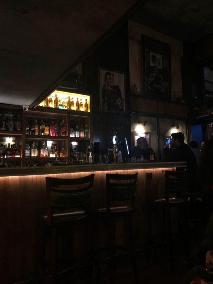 a dimly lit bar with several bottles on the shelves and people sitting at the bar