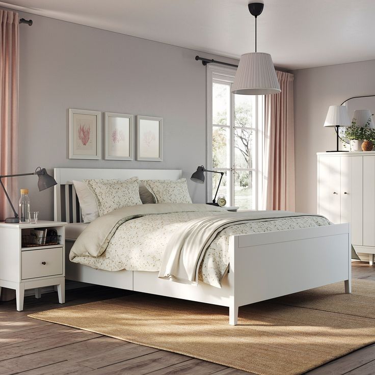 a white bed sitting in a bedroom next to a dresser and window with pink curtains