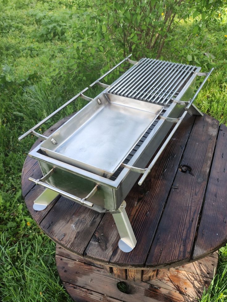 a grill sitting on top of a wooden table in the middle of some grass and trees