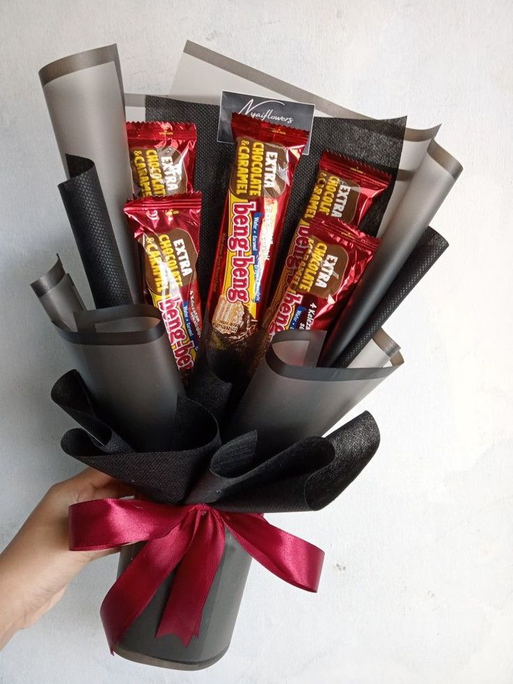 a hand holding a bunch of candy bars wrapped in black and red paper with a ribbon