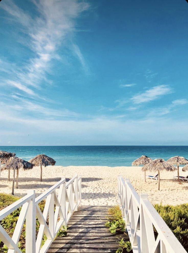 a wooden walkway leading to the beach with umbrellas and chairs in the sand behind it