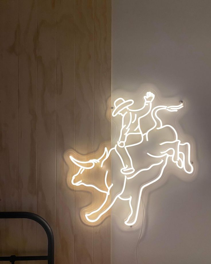 a neon sign with a cowboy riding a cow on it's back in front of a wooden wall