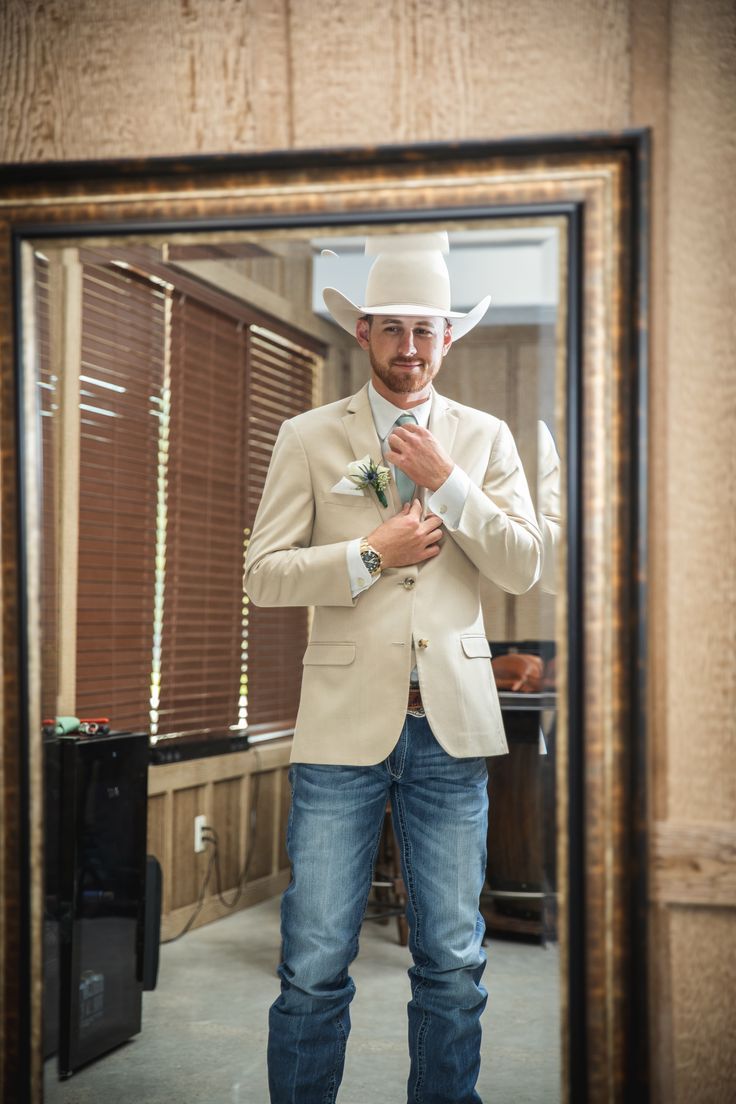 a man standing in front of a mirror wearing a white cowboy hat and blue jeans