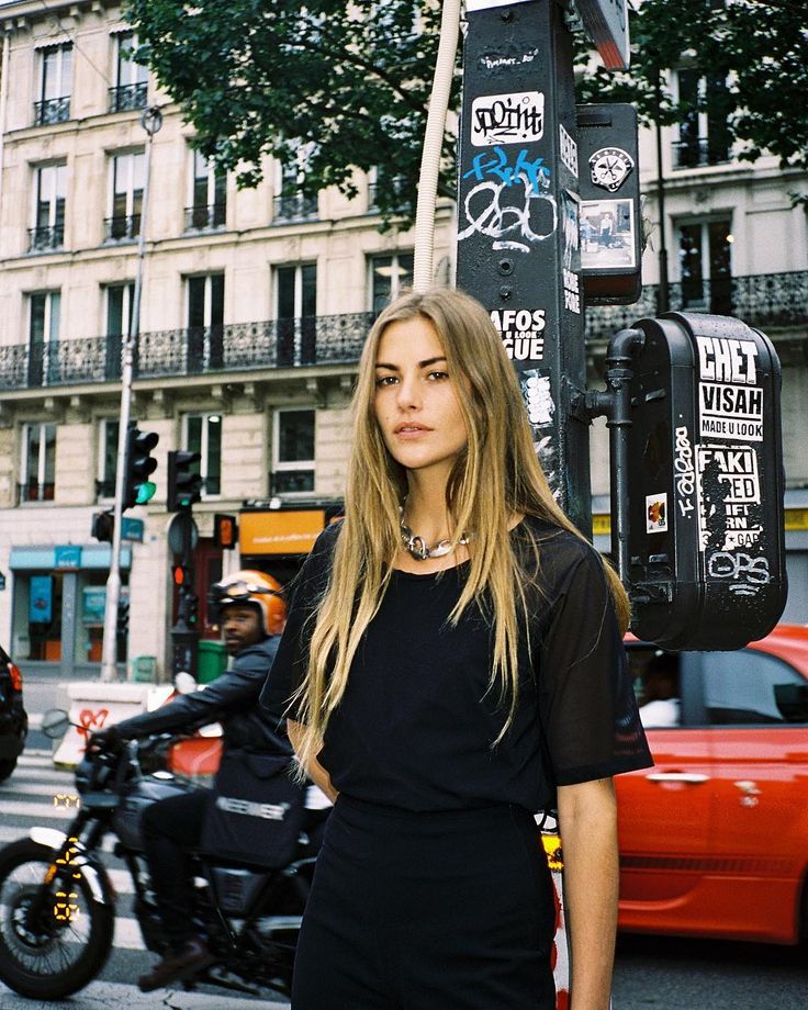 a woman standing next to a pole with graffiti on it in the middle of a city