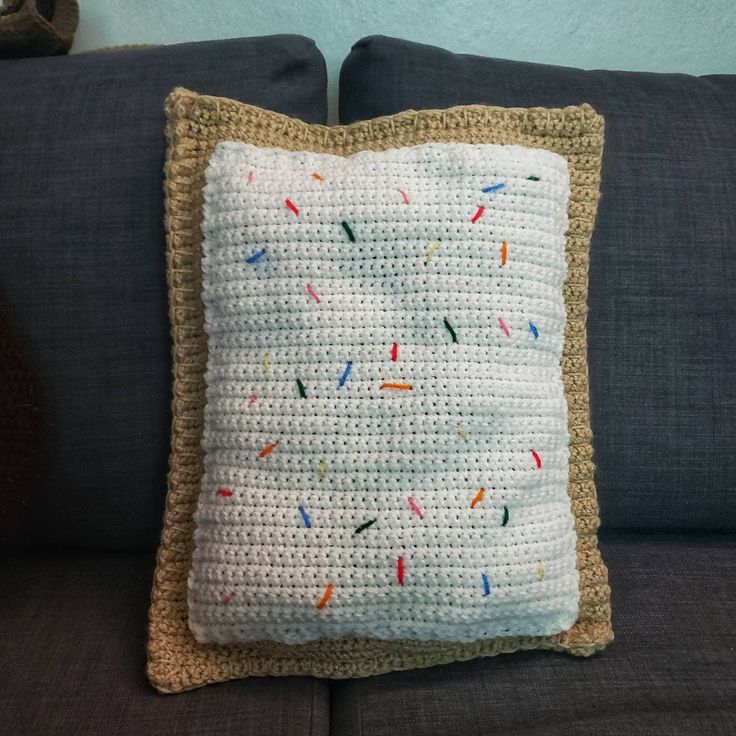 a crocheted pillow with sprinkles on it sitting on a couch