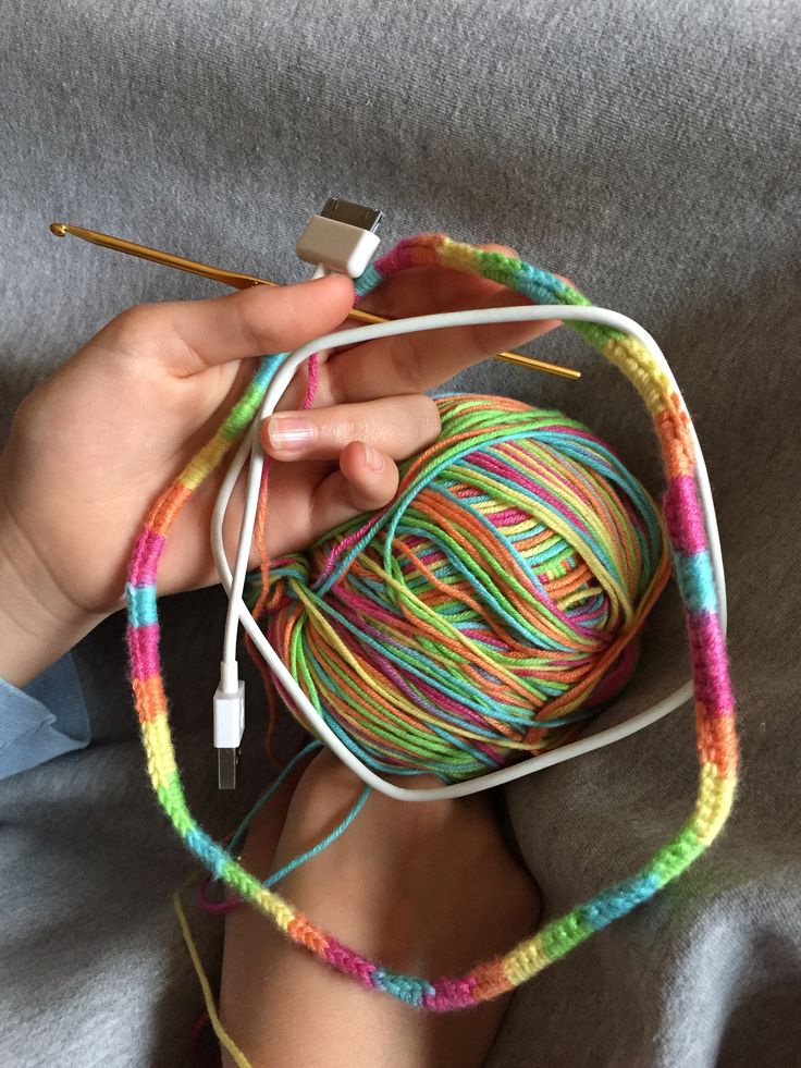 a person is knitting yarn with crochet needles and an iphone charger in their hand