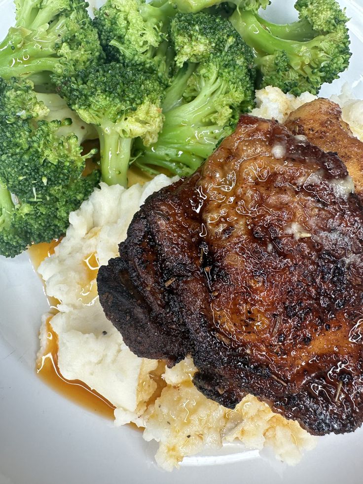 a white plate topped with meat and potatoes covered in gravy next to broccoli