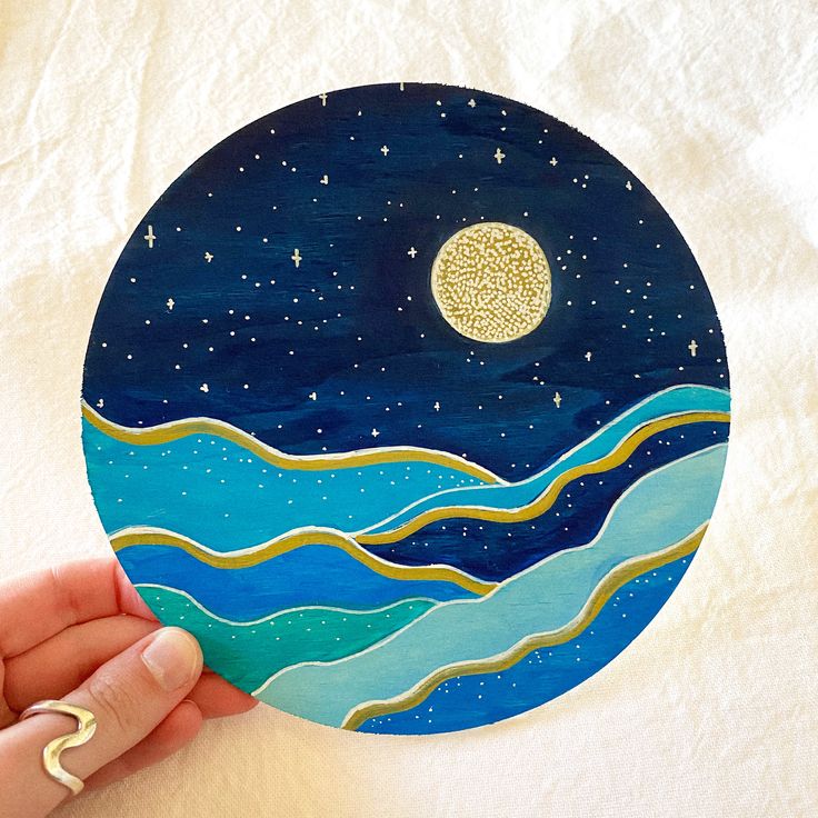 a hand holding up a painted paper plate with a moon and stars in the sky