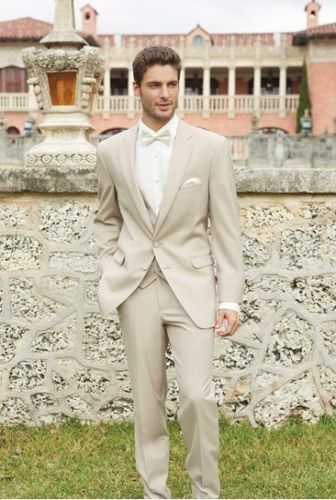 a man in a tuxedo standing next to a wall with a fountain behind him