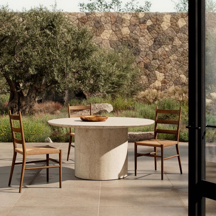 a table and chairs sitting on top of a cement floor next to an olive tree