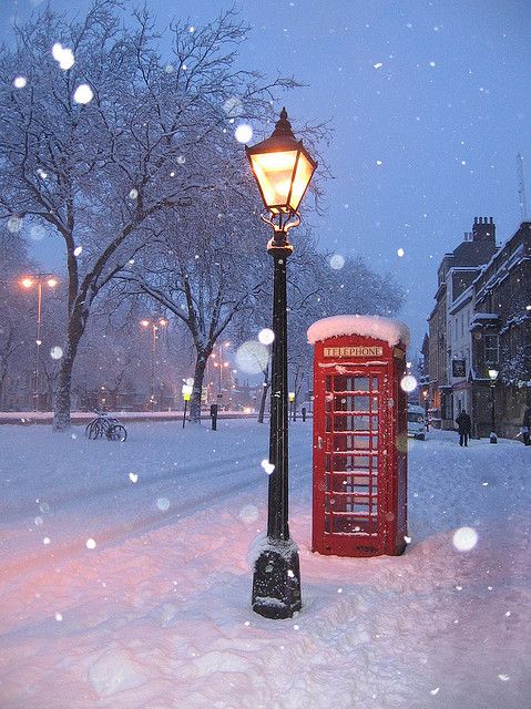 a red phone booth sitting in the middle of a snow covered park next to a lamp post