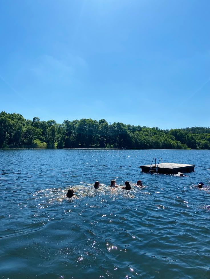 people swimming in the water near a boat on a lake with trees and blue sky