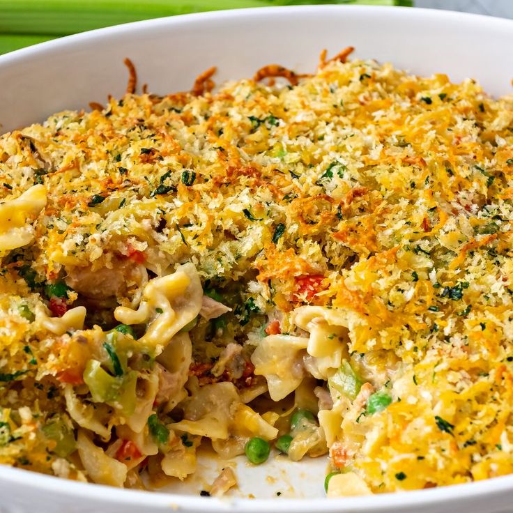 a casserole dish with noodles and vegetables in it on a plate next to celery sticks