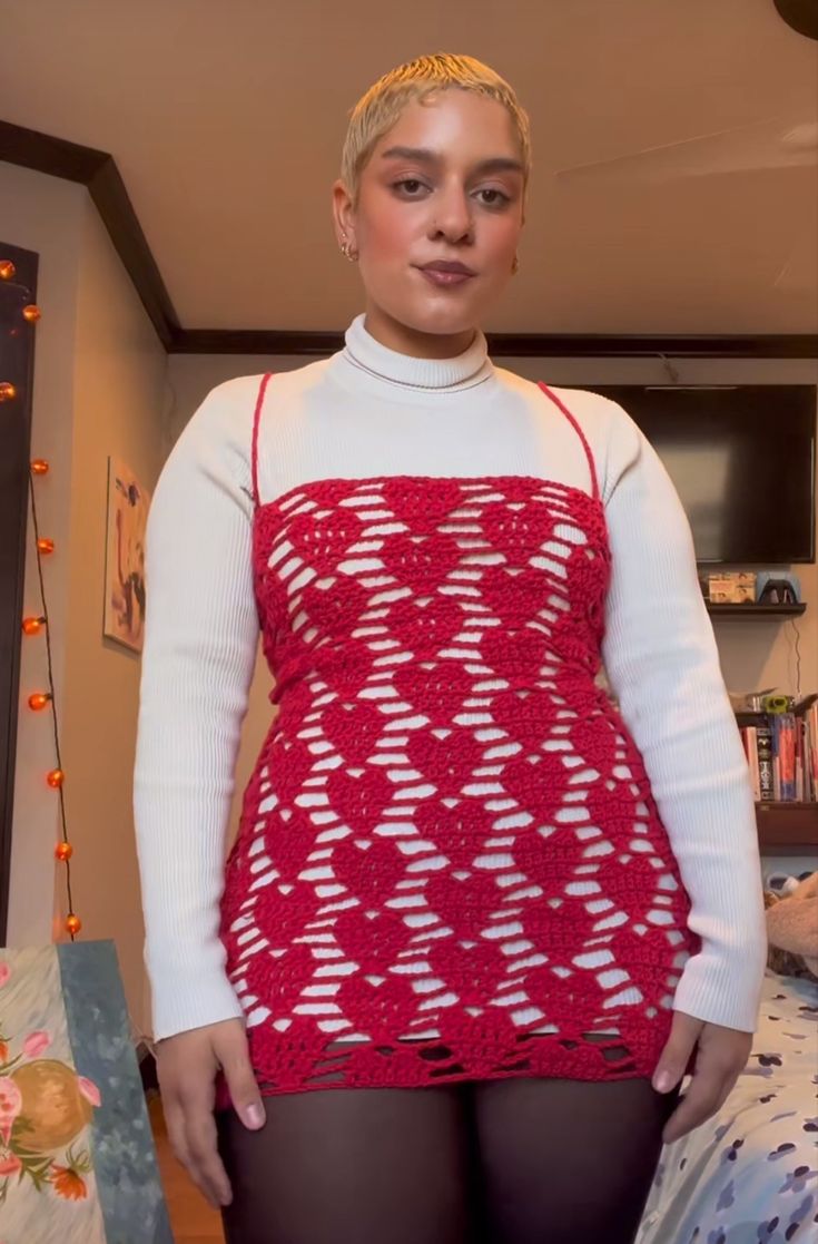 a woman with blonde hair wearing a red and white crochet dress standing in front of a bed