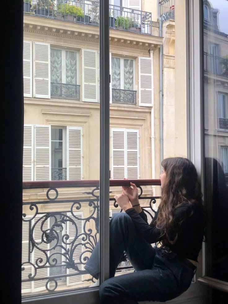 a woman sitting on top of a window sill looking out at the street below