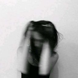 a blurry photo of a woman covering her face with her hands and standing in front of a wall