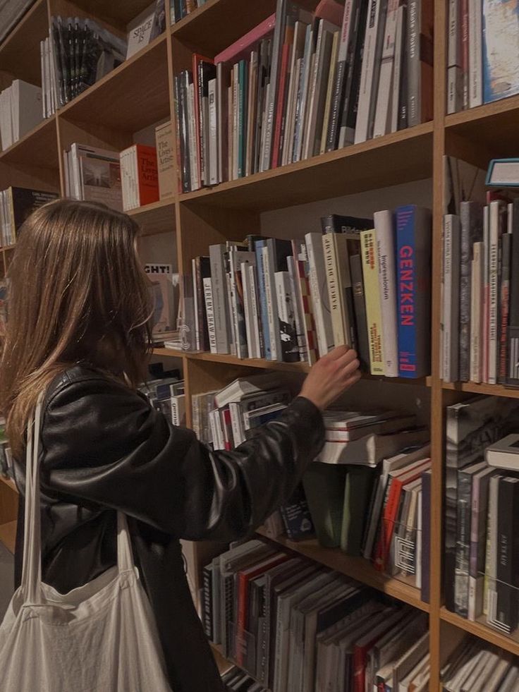 a woman looking at books on a book shelf in a library with shelves full of books