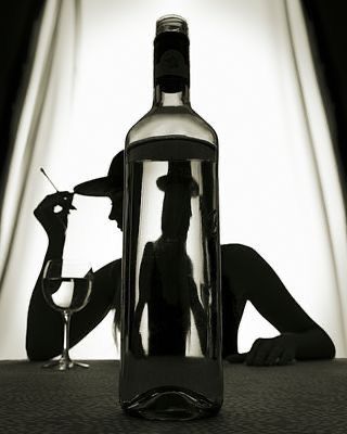 a woman sitting in front of a bottle of wine with a glass next to it