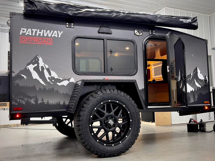 an off road camper trailer parked in a garage with the door open and mountains painted on it