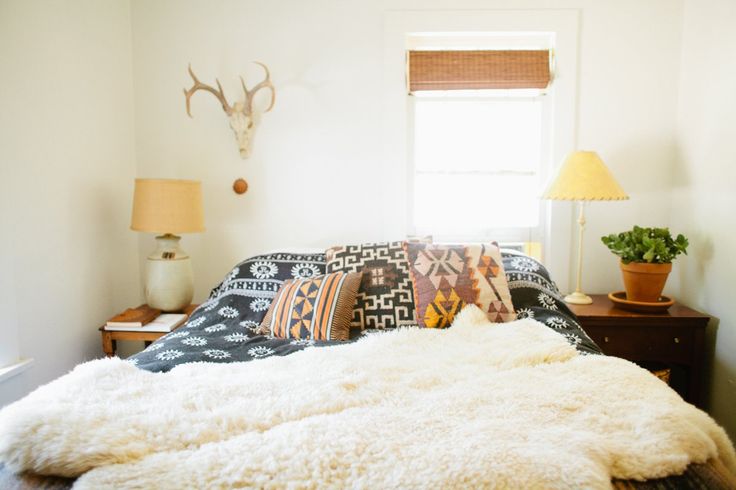 a bed with white fur on top of it and a lamp next to it in front of a window