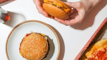 a person holding a hamburger in their hand next to a plate with pizza and soda