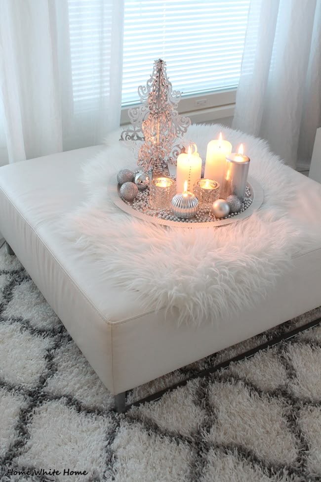 a white ottoman with candles on it in front of a window and a christmas tree