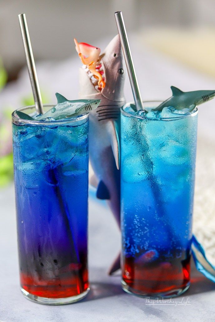 two glasses filled with blue liquid and shark toothpicks