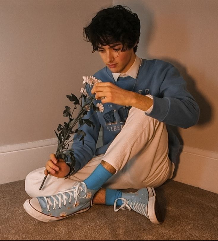 a young man sitting on the floor with flowers in his hand and wearing blue socks